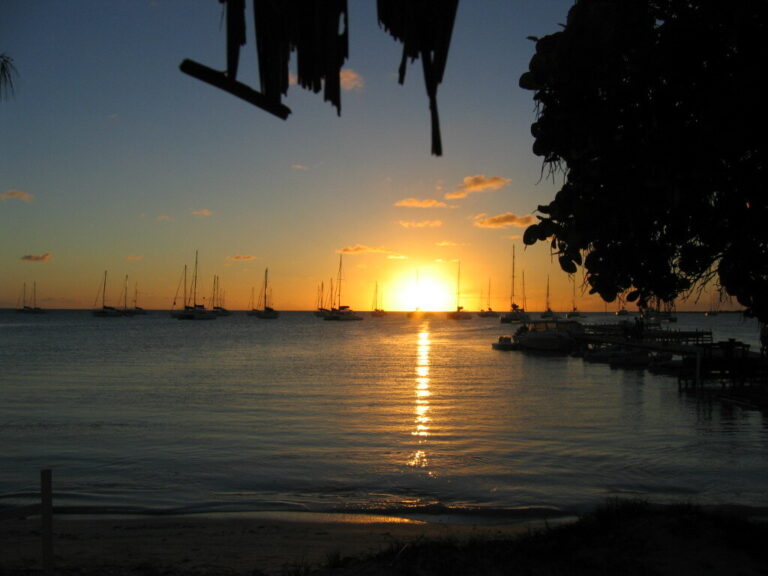 Sunset over a Caribbean mooring field, sailboats silhouetted against orange sky.