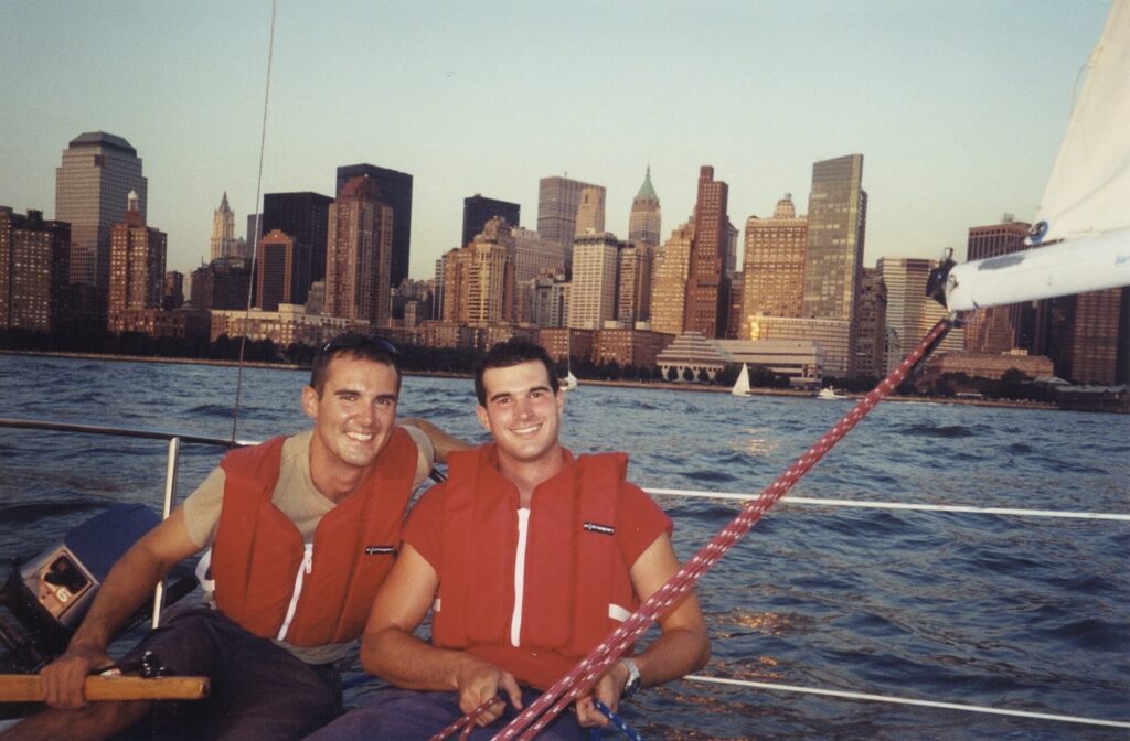 Two young crew members aboard a sailboat with the Manhattan skyline behind them, 2003