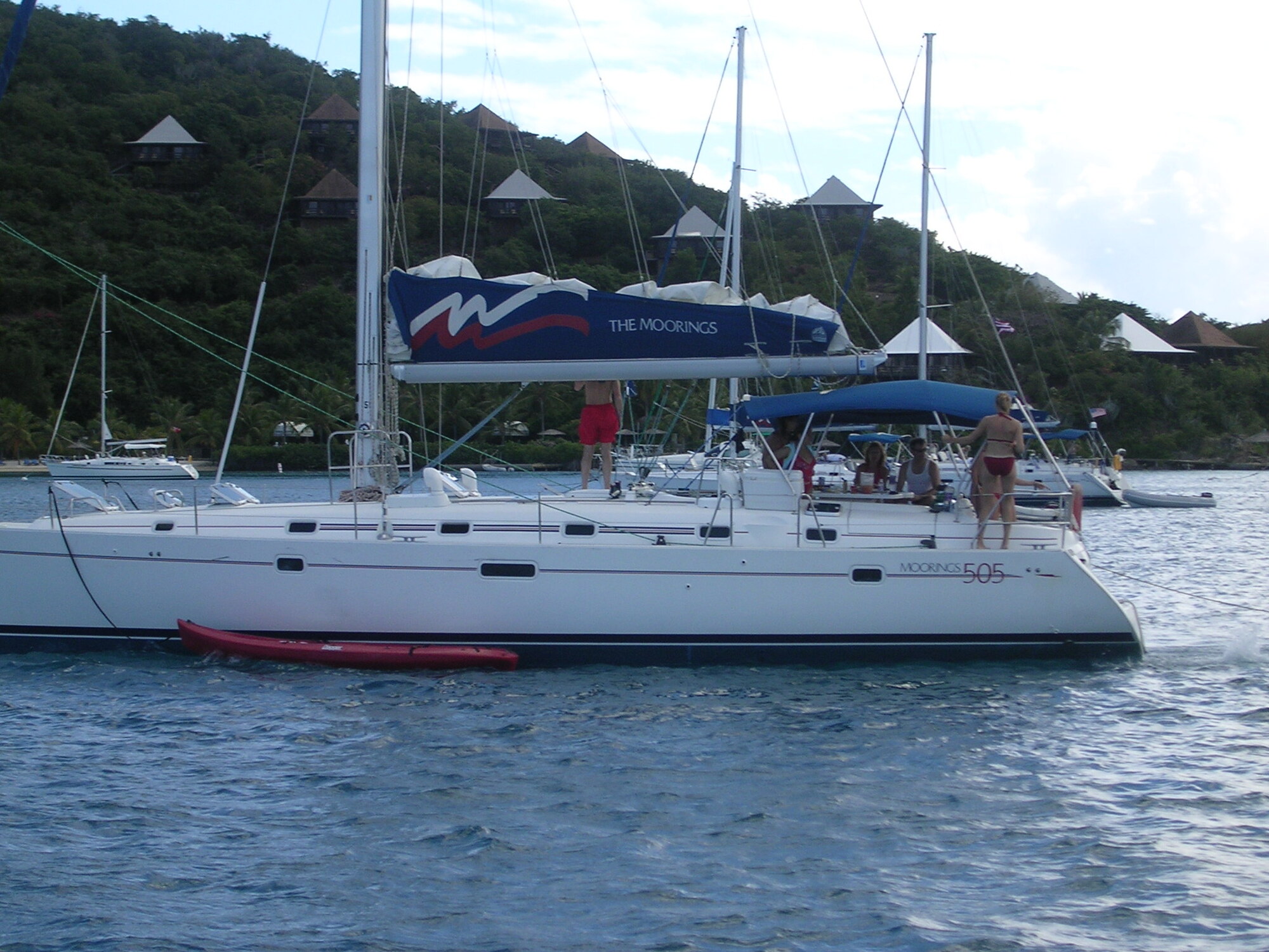 A Moorings charter catamaran under sail near a Virgin Islands hillside resort.